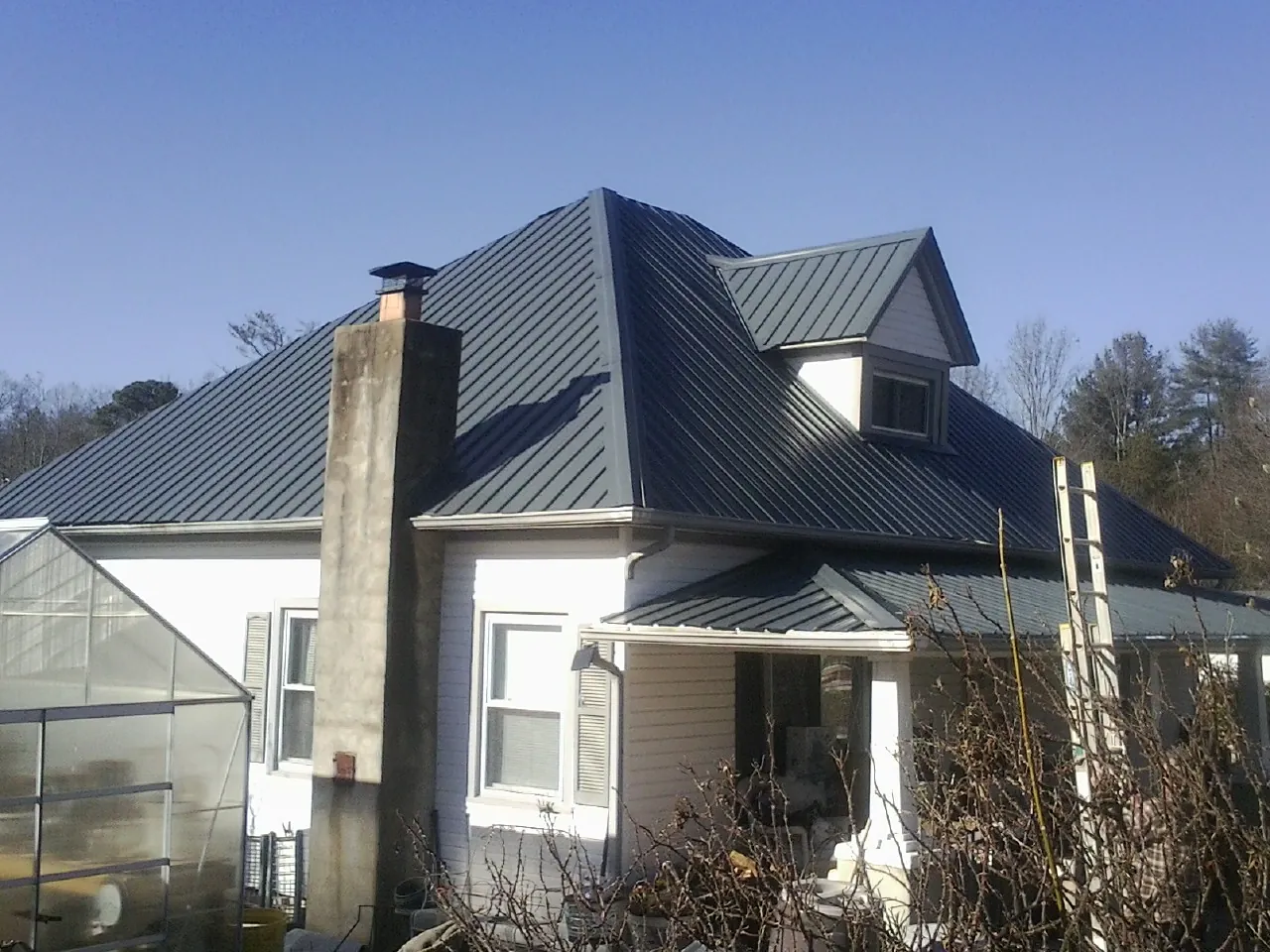 Dark blue standing seam metal roof on a white farmhouse with dormer — Slate & Tile Roof Repair by Roofing Brothers in Ninety Six
