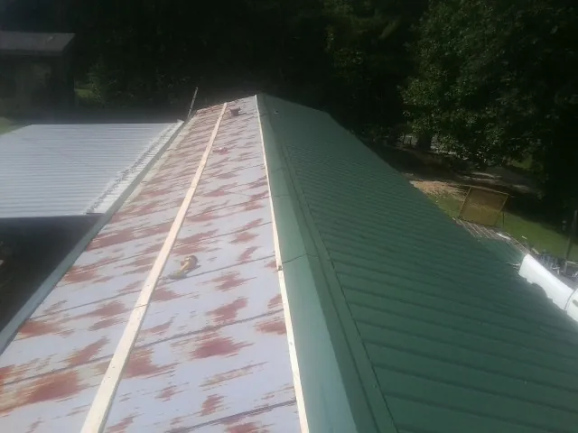 Old rusted panels beside newly installed green metal roofing — Wind Damage Roof Repair by Roofing Brothers in Ninety Six