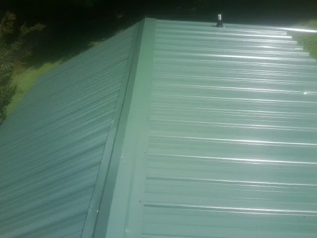 New green metal panels meeting at the ridge of a roof — Flat Roof Repair work by our crew in Ninety Six
