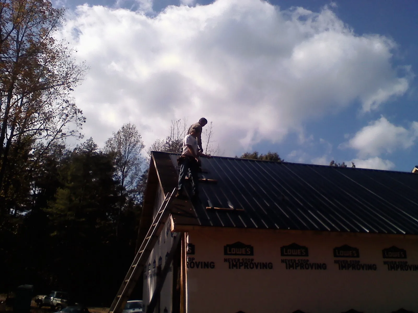 Roofer fastening dark metal panels high against a cloudy sky, from a Roof Inspection job in Ninety Six