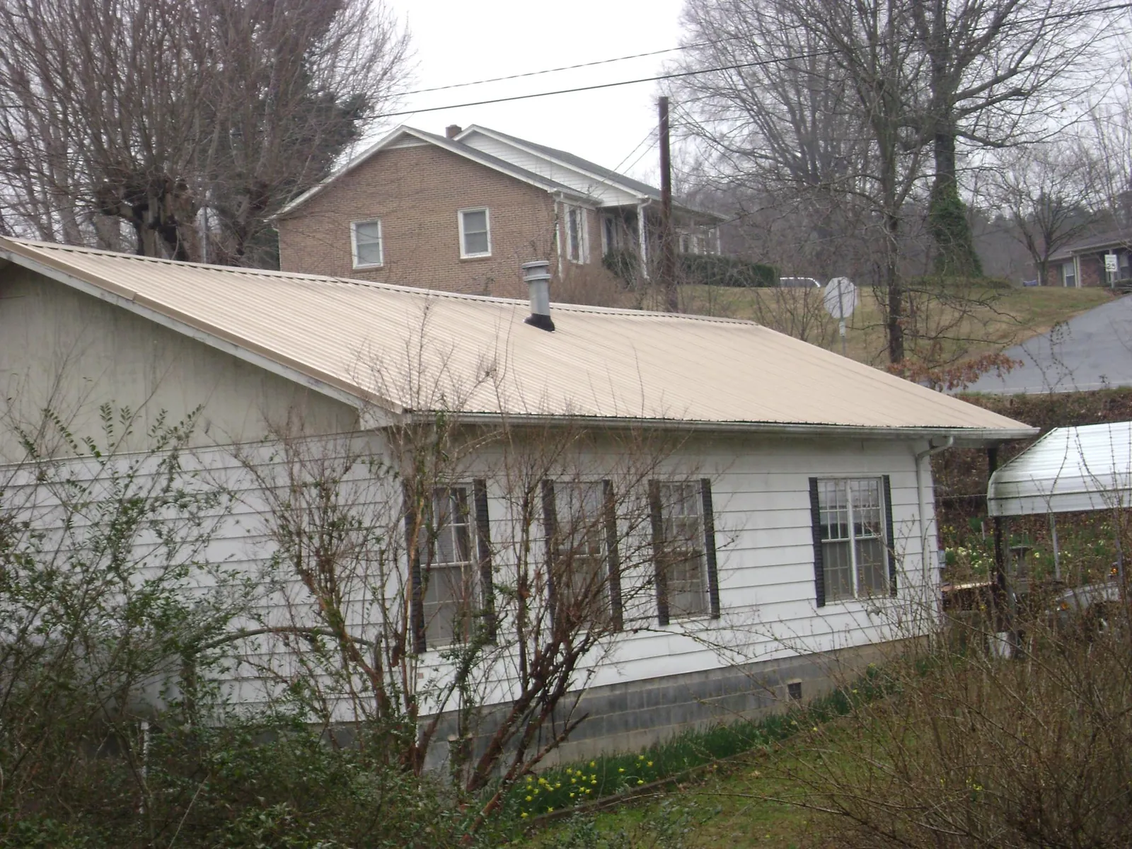 Tan metal roof on a white sided house set into a hillside — Commercial Roofing by Roofing Brothers in Ninety Six
